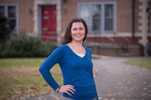 Woman in blue long-sleeve shirt standing in front of Gabriel House on Muhlenberg College campus.